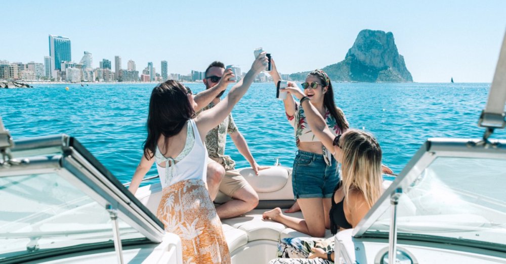 A group of adults gathered together on a boat that is sailing on the water during the day. Everyone is holding a can and toasting.